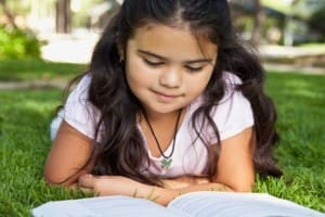 Hispanic girl laying in grass reading book